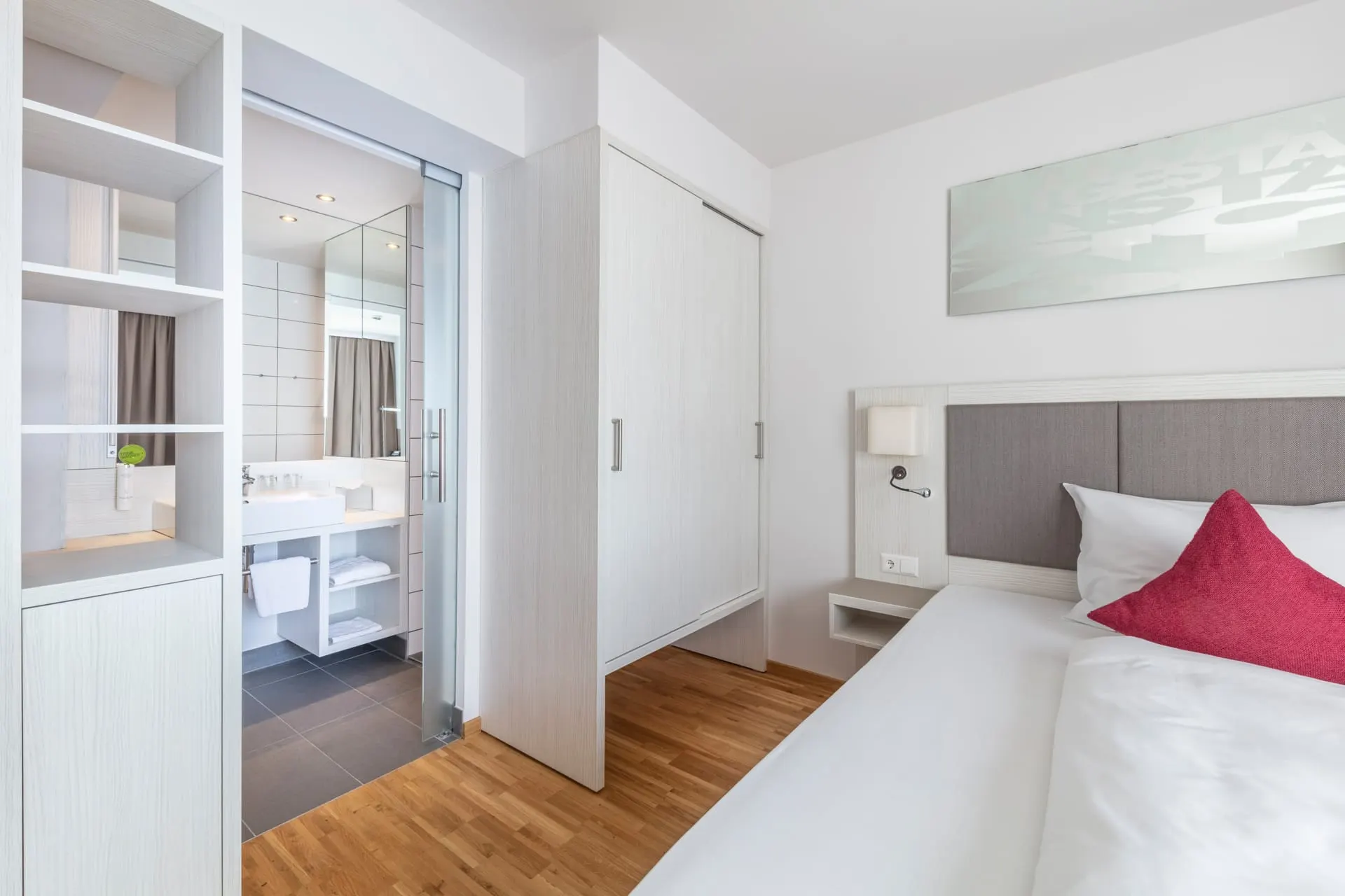 Zimmer City: Doppelbett mit roten Kissen, Schrank und Blick ins Bad