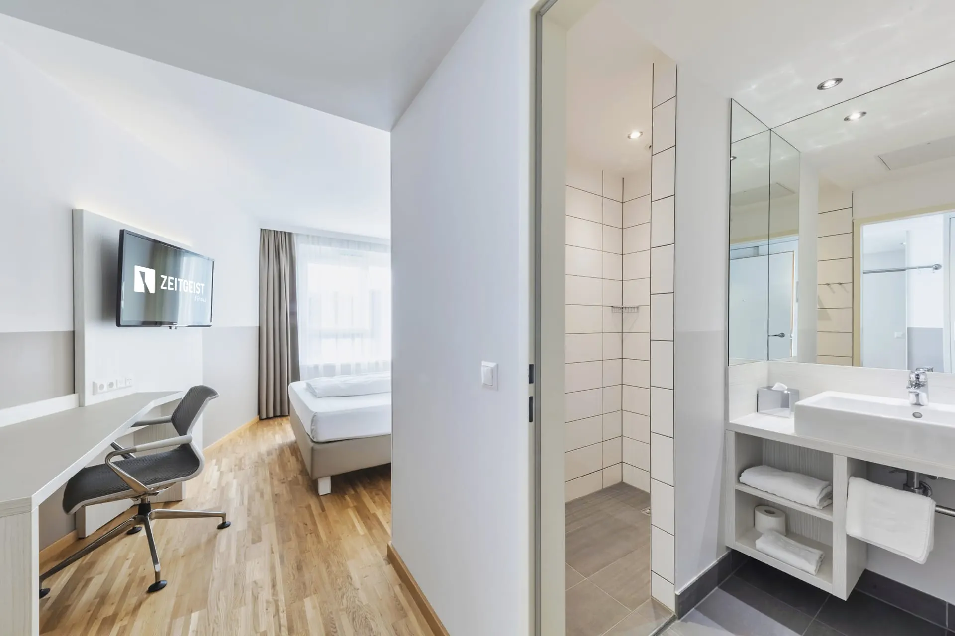 Zimmer Urban: Schreibtisch und Bett, rechts das Bad mit Dusche und Waschtisch