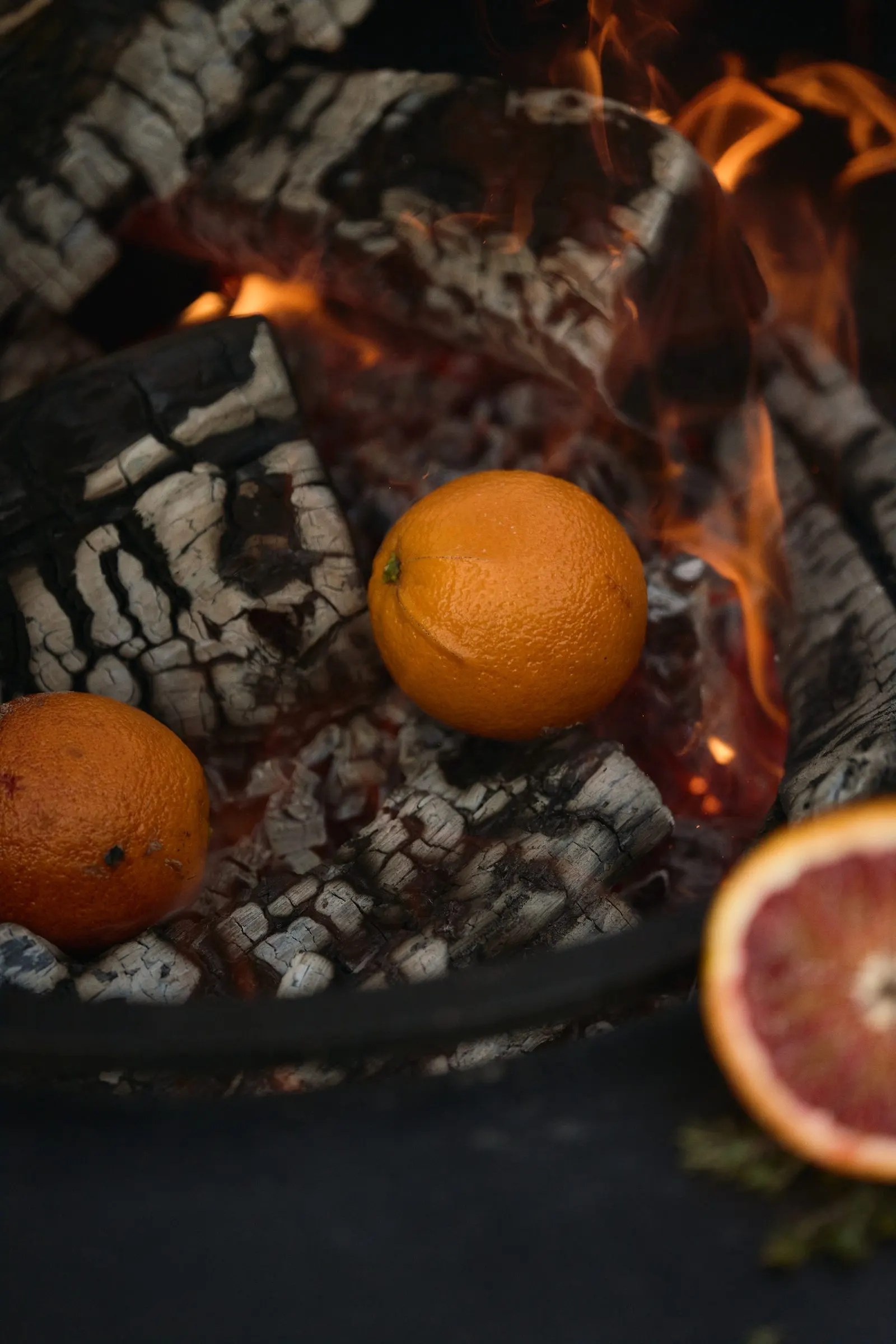 Glühende Holzscheite im OFYR, dazwischen Orangen und eine Blutorange