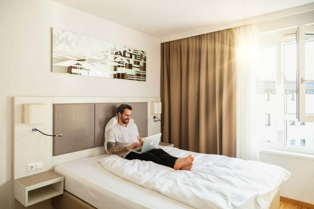 Guest lies in bed of room category City and works on laptop